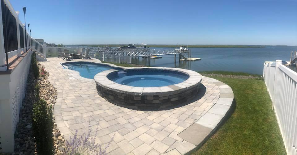 A round pool and patio next to a large body of water.